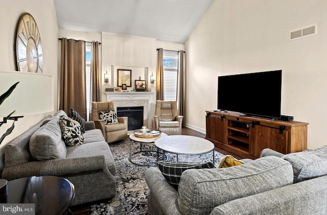 living area with vaulted ceiling, visible vents, wood finished floors, baseboards, and a glass covered fireplace