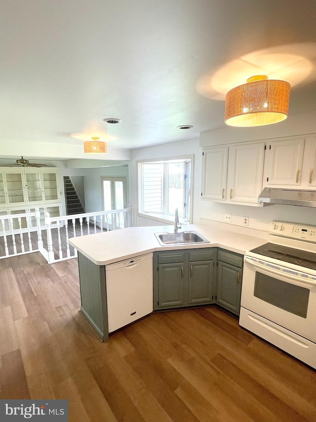 kitchen featuring white appliances, a peninsula, under cabinet range hood, a sink, and wood finished floors