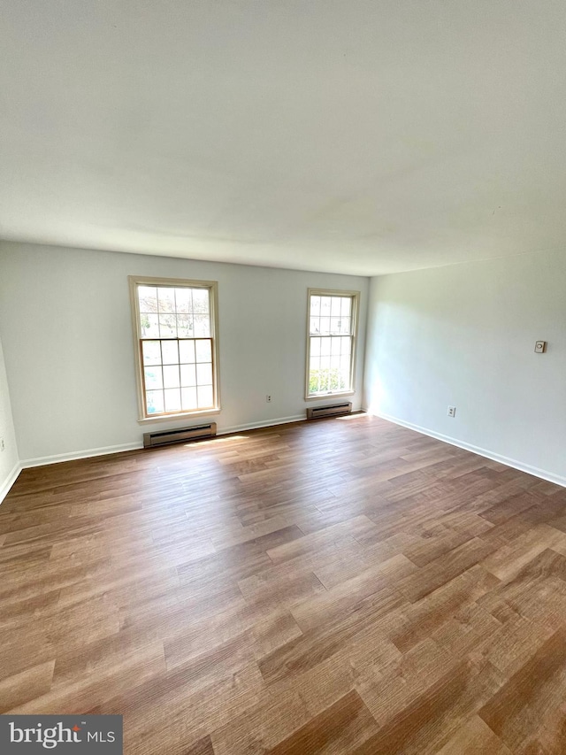 empty room featuring wood finished floors, a baseboard heating unit, and baseboards