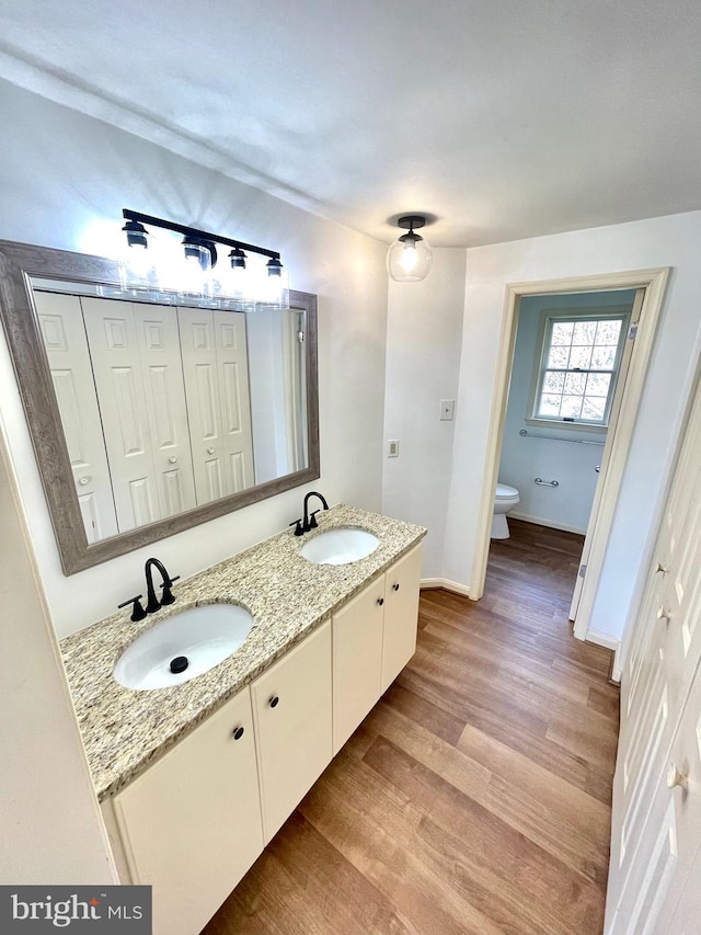 full bath featuring double vanity, a sink, toilet, and wood finished floors
