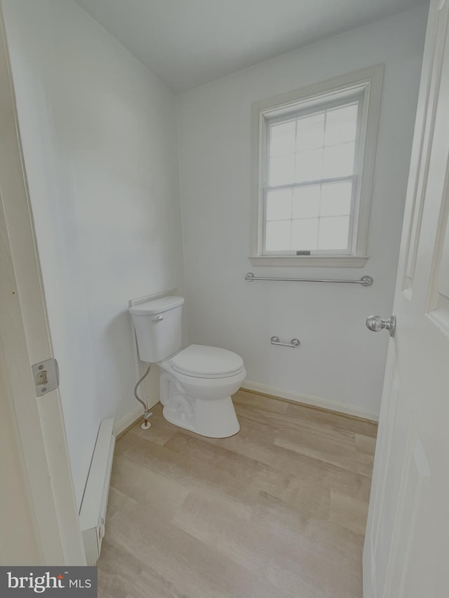 bathroom featuring toilet, wood finished floors, a baseboard heating unit, and baseboards
