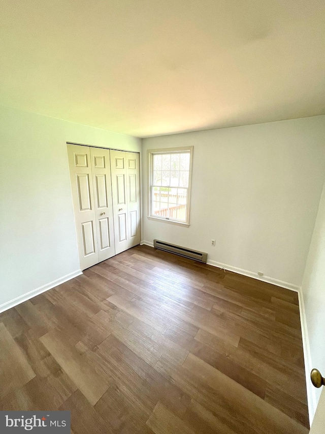 unfurnished bedroom featuring a closet, dark wood-type flooring, a baseboard heating unit, and baseboards