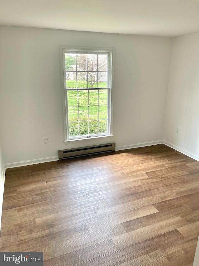 empty room featuring a baseboard radiator, wood finished floors, and baseboards