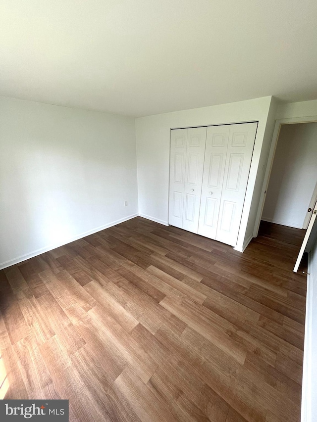 unfurnished bedroom featuring wood finished floors, a closet, and baseboards