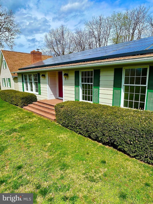 single story home featuring roof mounted solar panels, a front yard, and a chimney