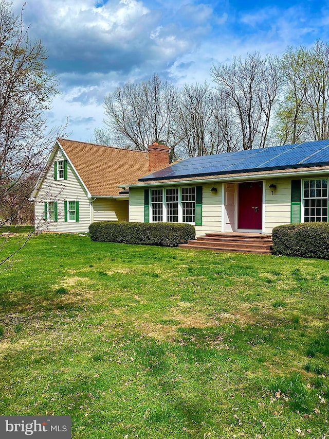 ranch-style home featuring a front lawn, solar panels, and a chimney