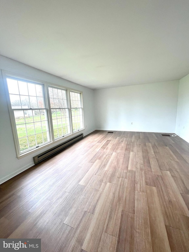unfurnished room featuring a baseboard radiator, plenty of natural light, and wood finished floors
