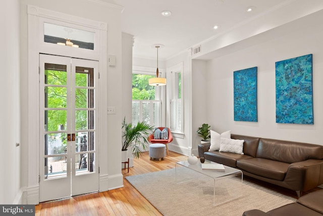 living area with hardwood / wood-style flooring, visible vents, baseboards, ornamental molding, and french doors