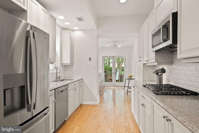 kitchen featuring a sink, stainless steel appliances, decorative backsplash, visible vents, and white cabinets