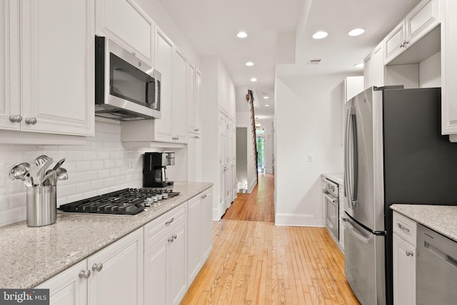 kitchen with light wood finished floors, appliances with stainless steel finishes, decorative backsplash, and white cabinetry