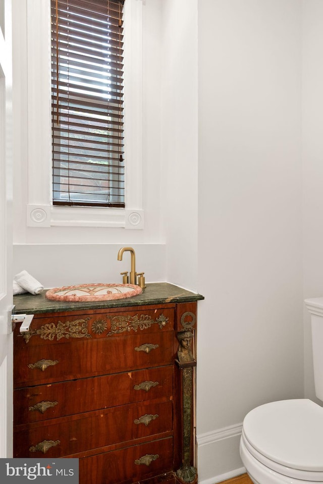 half bath with baseboards, toilet, and vanity