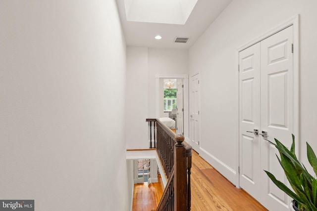 hall with an upstairs landing, visible vents, light wood-style floors, recessed lighting, and a skylight