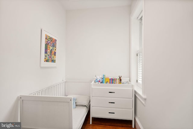 bedroom featuring dark wood-style floors and a crib
