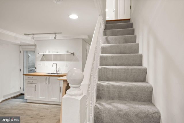 stairs with recessed lighting, ornamental molding, rail lighting, wood finished floors, and wet bar