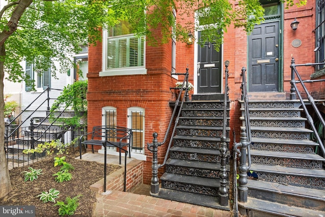 view of exterior entry with fence and brick siding