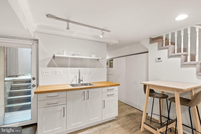 kitchen with a sink, open shelves, light wood-style flooring, white cabinetry, and butcher block counters