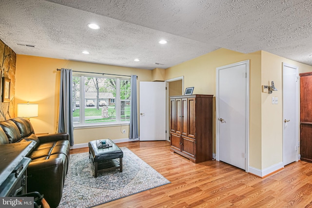 living area featuring recessed lighting, visible vents, light wood-type flooring, baseboards, and a textured ceiling