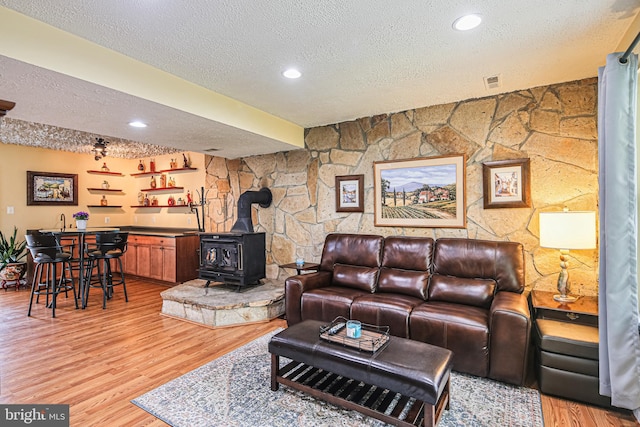 living room featuring a wood stove, a textured ceiling, visible vents, and light wood-style floors