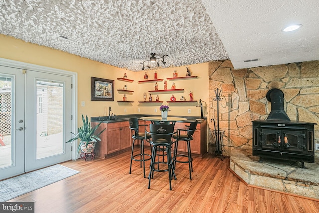 dining area featuring french doors, light wood-style flooring, a textured ceiling, wet bar, and a wood stove