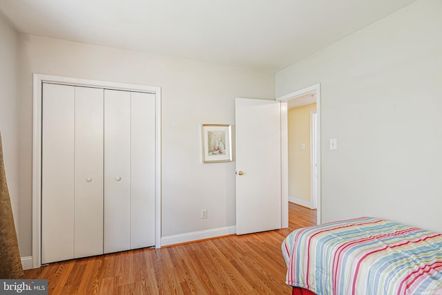 bedroom with light wood-style flooring, baseboards, and a closet