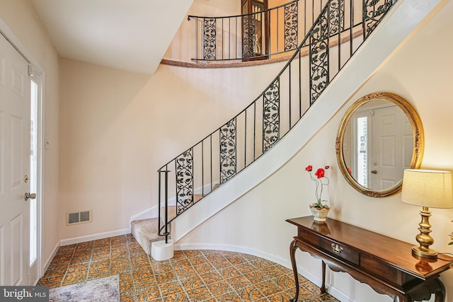 entrance foyer with stairway, a high ceiling, baseboards, and visible vents