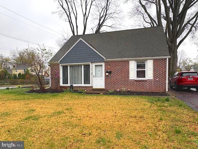 view of front of property with brick siding, a shingled roof, and a front lawn
