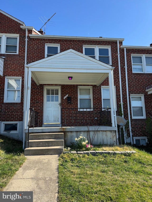 view of property with a porch, a front yard, and brick siding