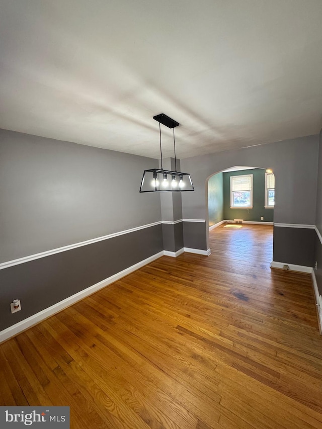 unfurnished dining area featuring baseboards, arched walkways, and wood finished floors