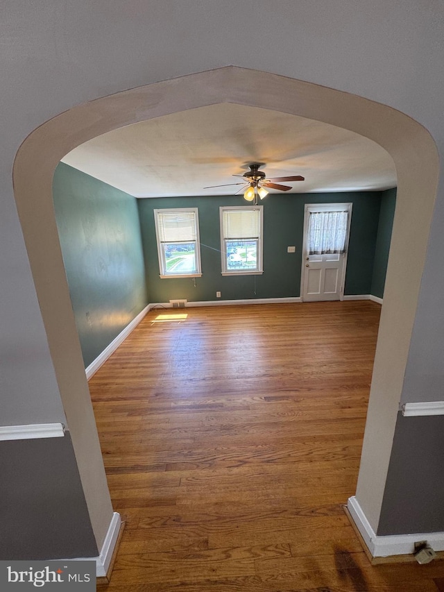 unfurnished room with arched walkways, wood finished floors, and a healthy amount of sunlight