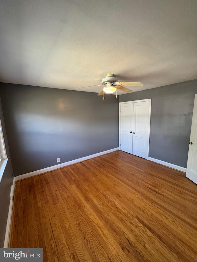 unfurnished bedroom with a closet, baseboards, ceiling fan, and wood finished floors