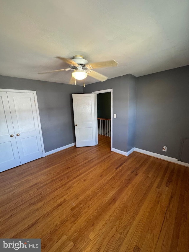 unfurnished bedroom with a closet, baseboards, a ceiling fan, and wood finished floors