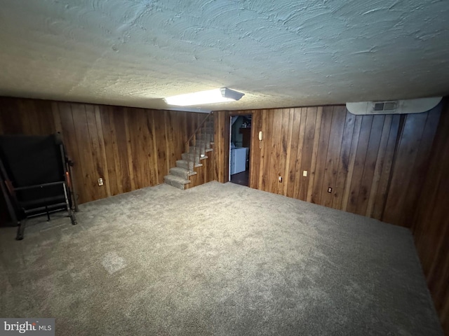 finished below grade area with wood walls, stairway, carpet, and a textured ceiling