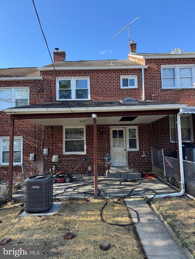 back of house featuring brick siding, central air condition unit, covered porch, and a chimney