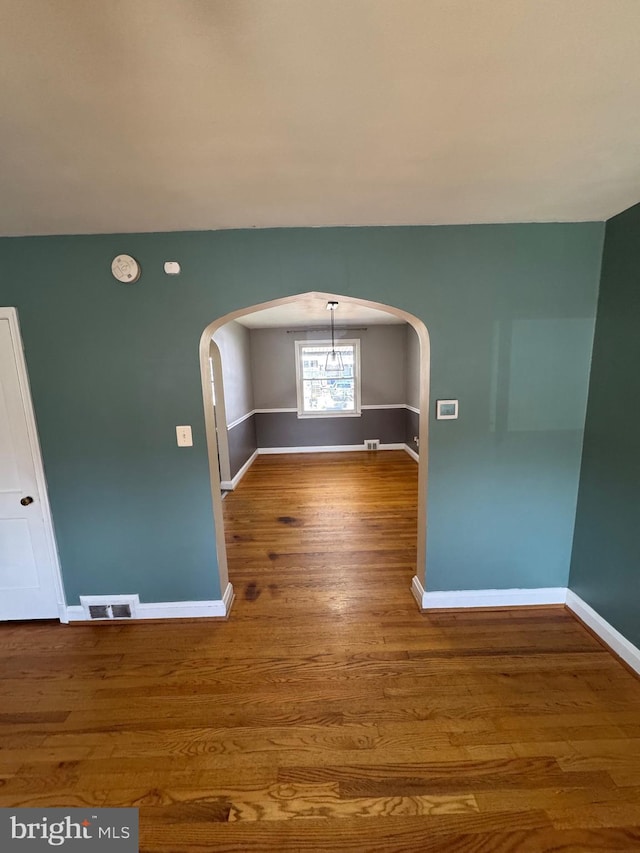 spare room featuring baseboards, arched walkways, and wood finished floors