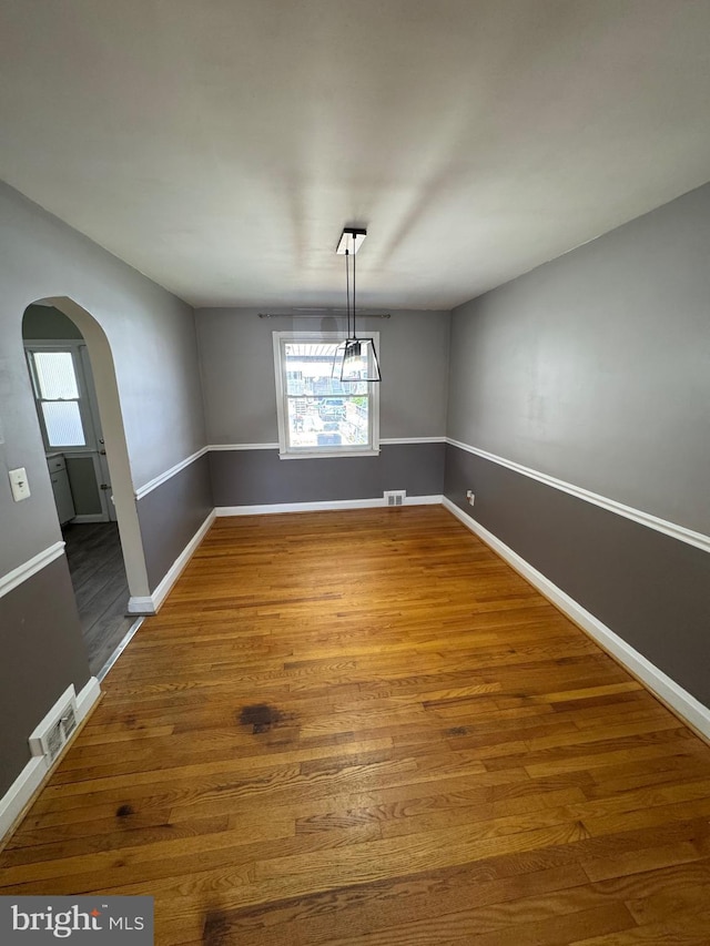 unfurnished dining area featuring baseboards, arched walkways, plenty of natural light, and wood finished floors