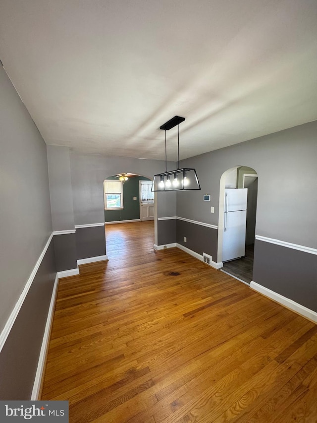 unfurnished dining area with ceiling fan, arched walkways, wood finished floors, and baseboards
