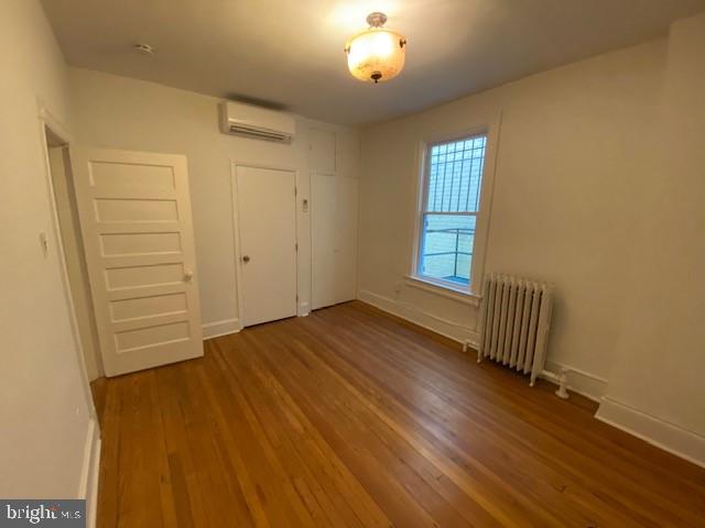 1674 Irving St NW, Washington, DC 20010 - unfurnished bedroom with baseboards, a wall mounted AC, wood finished floors, and radiator