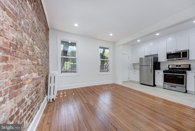 1674 Irving St NW, Washington, DC 20010 - kitchen featuring light wood-type flooring, baseboards, radiator heating unit, stainless steel appliances, and white cabinetry