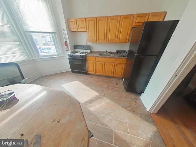 kitchen featuring baseboards, a sink, light countertops, freestanding refrigerator, and gas range oven