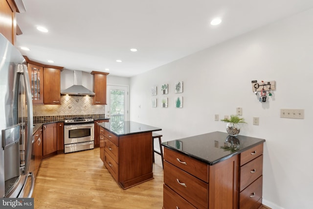 kitchen with appliances with stainless steel finishes, a center island, light wood finished floors, wall chimney exhaust hood, and brown cabinetry