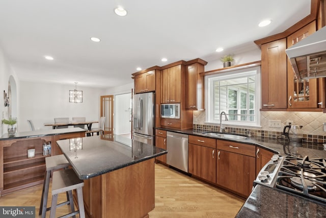 kitchen featuring dark stone countertops, stainless steel appliances, backsplash, a sink, and wall chimney exhaust hood