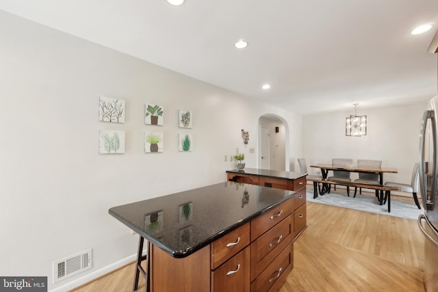 kitchen featuring arched walkways, a kitchen island, light wood finished floors, visible vents, and a kitchen breakfast bar