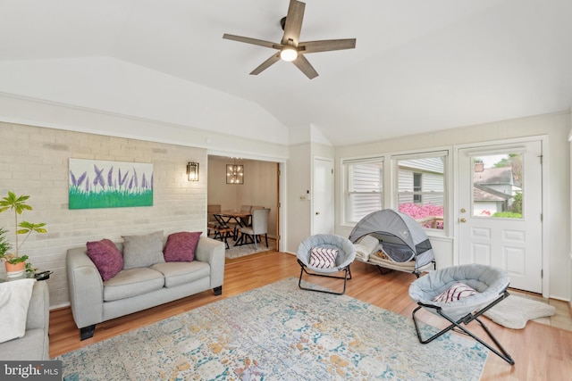 living room with lofted ceiling, brick wall, wood finished floors, and ceiling fan