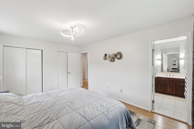 bedroom featuring connected bathroom, a sink, light wood-style floors, baseboards, and multiple closets
