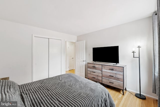 bedroom with a closet, light wood-style flooring, and baseboards