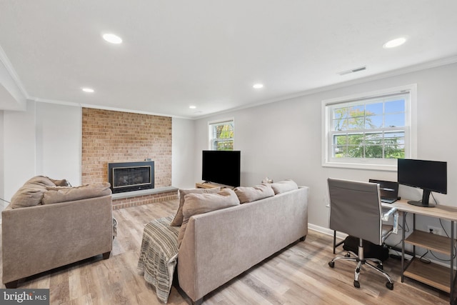living room with visible vents, light wood-type flooring, ornamental molding, and a brick fireplace