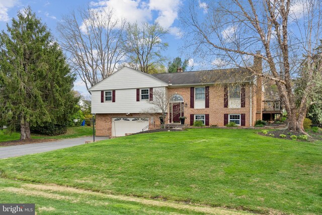 bi-level home with a front yard, a garage, a chimney, driveway, and brick siding