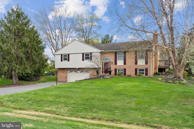 split foyer home with driveway, a chimney, brick siding, a front lawn, and a garage