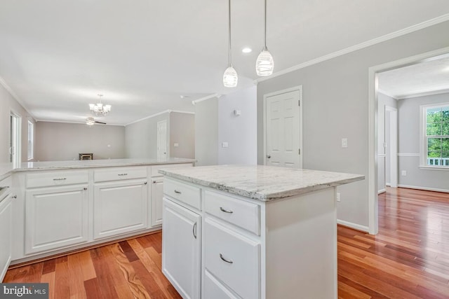 kitchen with crown molding, light wood finished floors, a kitchen island, a chandelier, and pendant lighting
