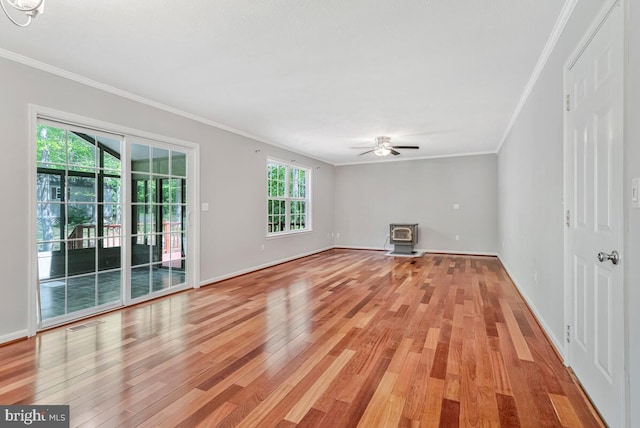 unfurnished living room featuring a wood stove, ornamental molding, light wood finished floors, a ceiling fan, and baseboards